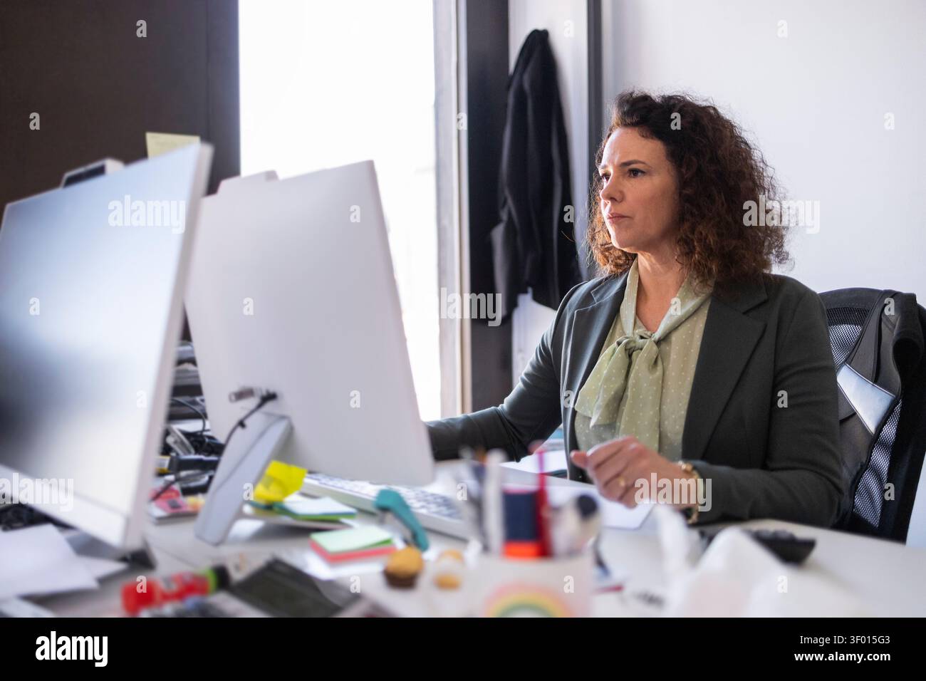 Donna professionista in abbigliamento da lavoro che lavora con un computer desktop in un moderno ambiente di lavoro, concentrata sulle attività e sulla produttività, con monitor, no Foto Stock
