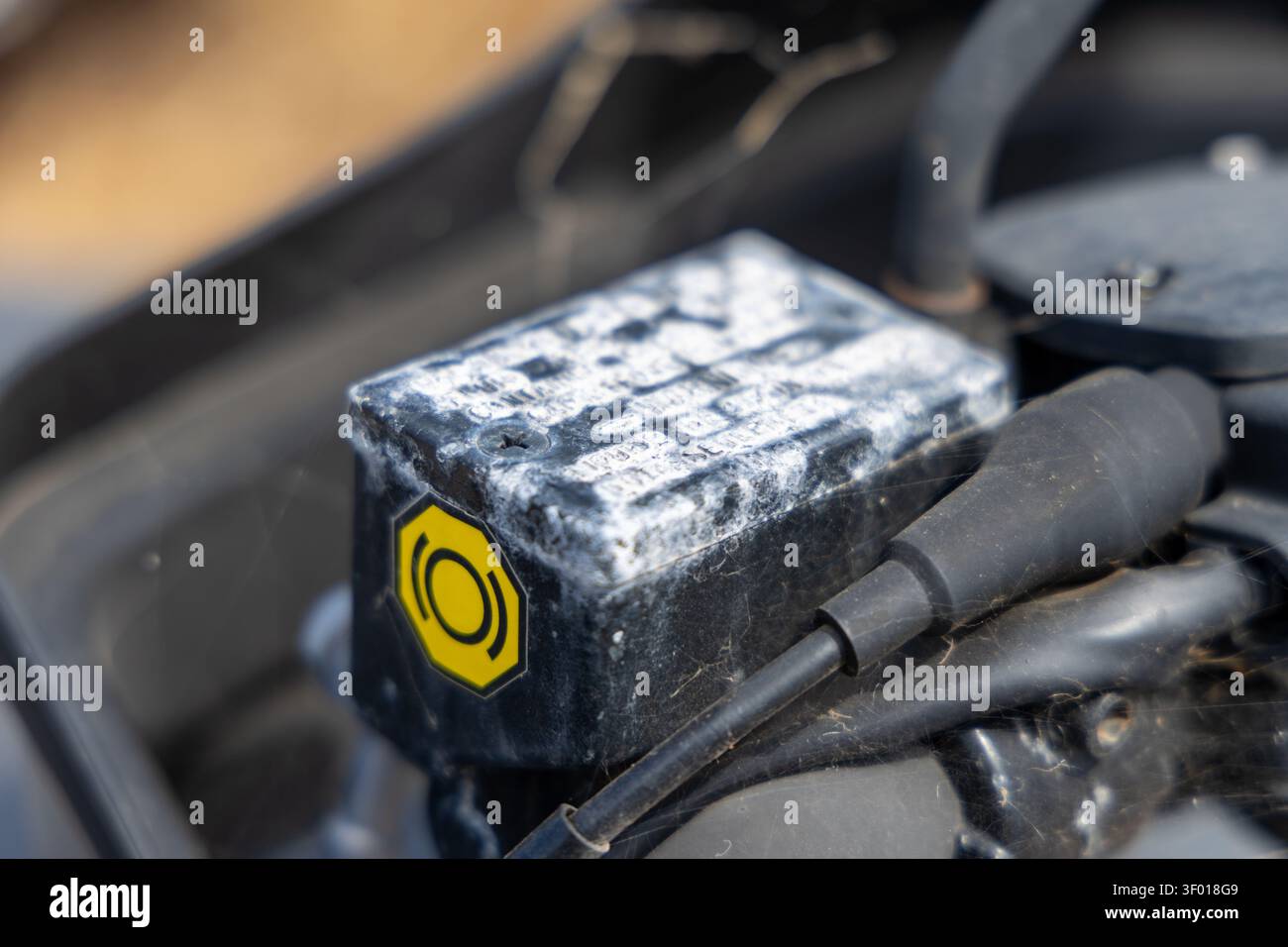 Questa immagine dettagliata si concentra su un serbatoio del liquido dei freni usurato, con un adesivo di avvertenza giallo e segni di età e utilizzo sui componenti del motore di un veicolo Foto Stock