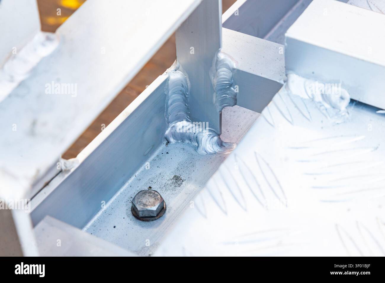 Primo piano di cordoni di saldatura in alluminio su una struttura industriale in metallo con struttura a piastra diamantata e bullone in acciaio Foto Stock