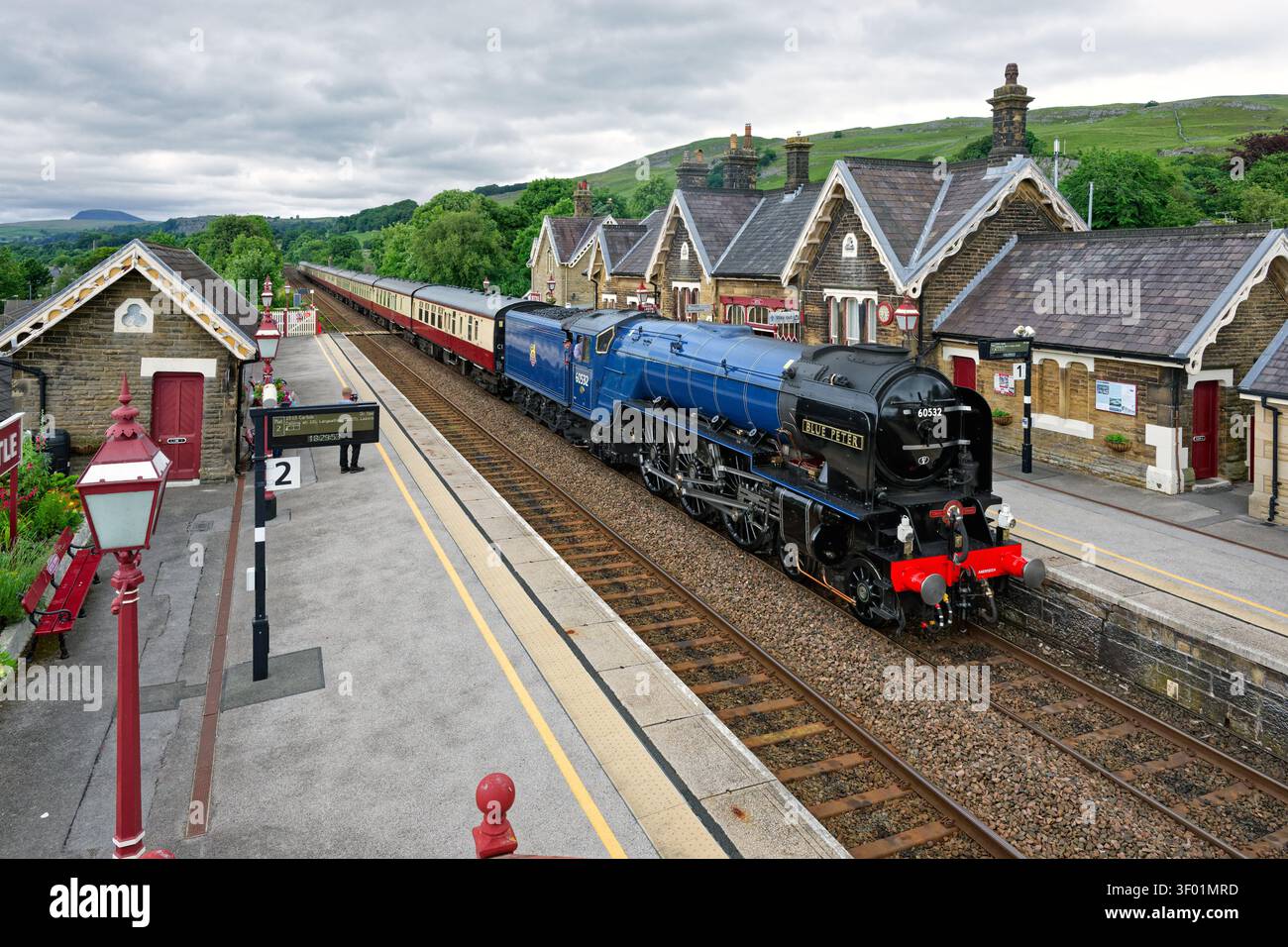 La locomotiva a vapore "Blue Peter" fa una sosta per l'acqua alla stazione di Settle durante il viaggio di ritorno da Carlisle Foto Stock