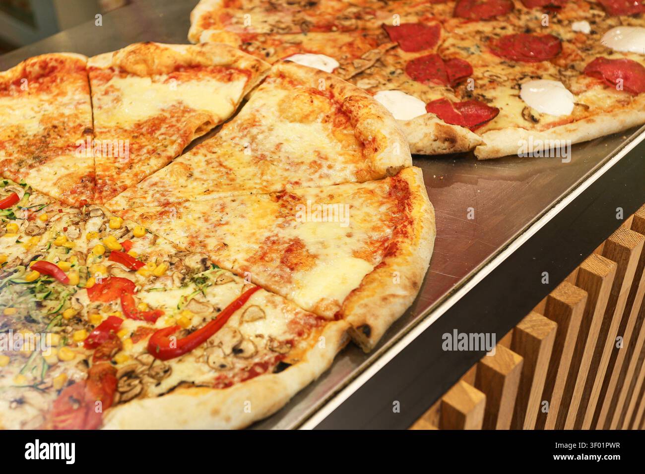 Pizze appena sfornate esposte sul bancone con vari condimenti. Sfondo di cibo italiano per pasti da asporto, pranzo, cena, fast food e pasti informali. Foto Stock