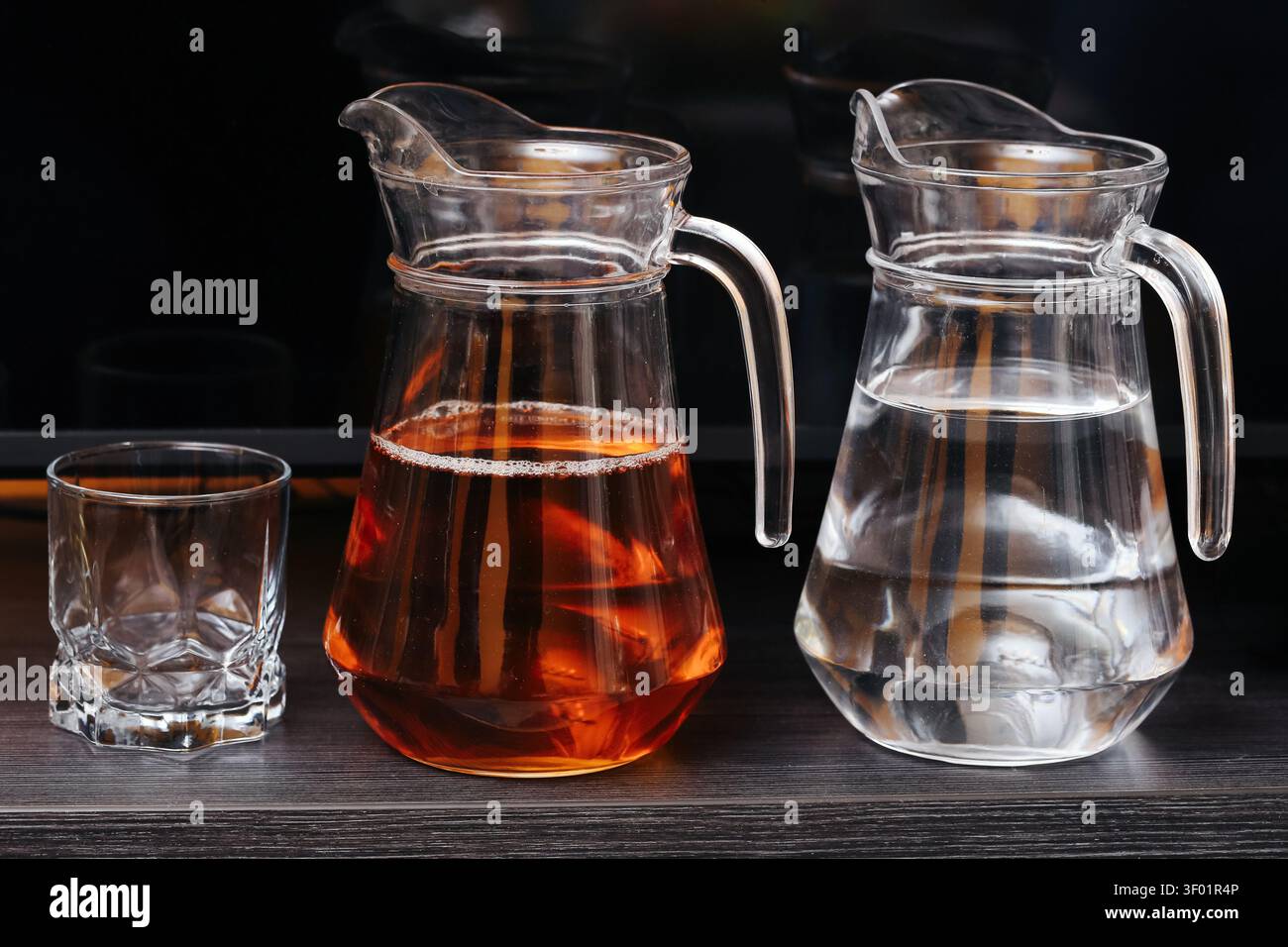 Bicchieri di vetro con acqua e bevanda ambrata accanto a un bicchiere vuoto. Sfondo di bevande per il servizio di ristorazione con rinfresco idratante. Foto Stock