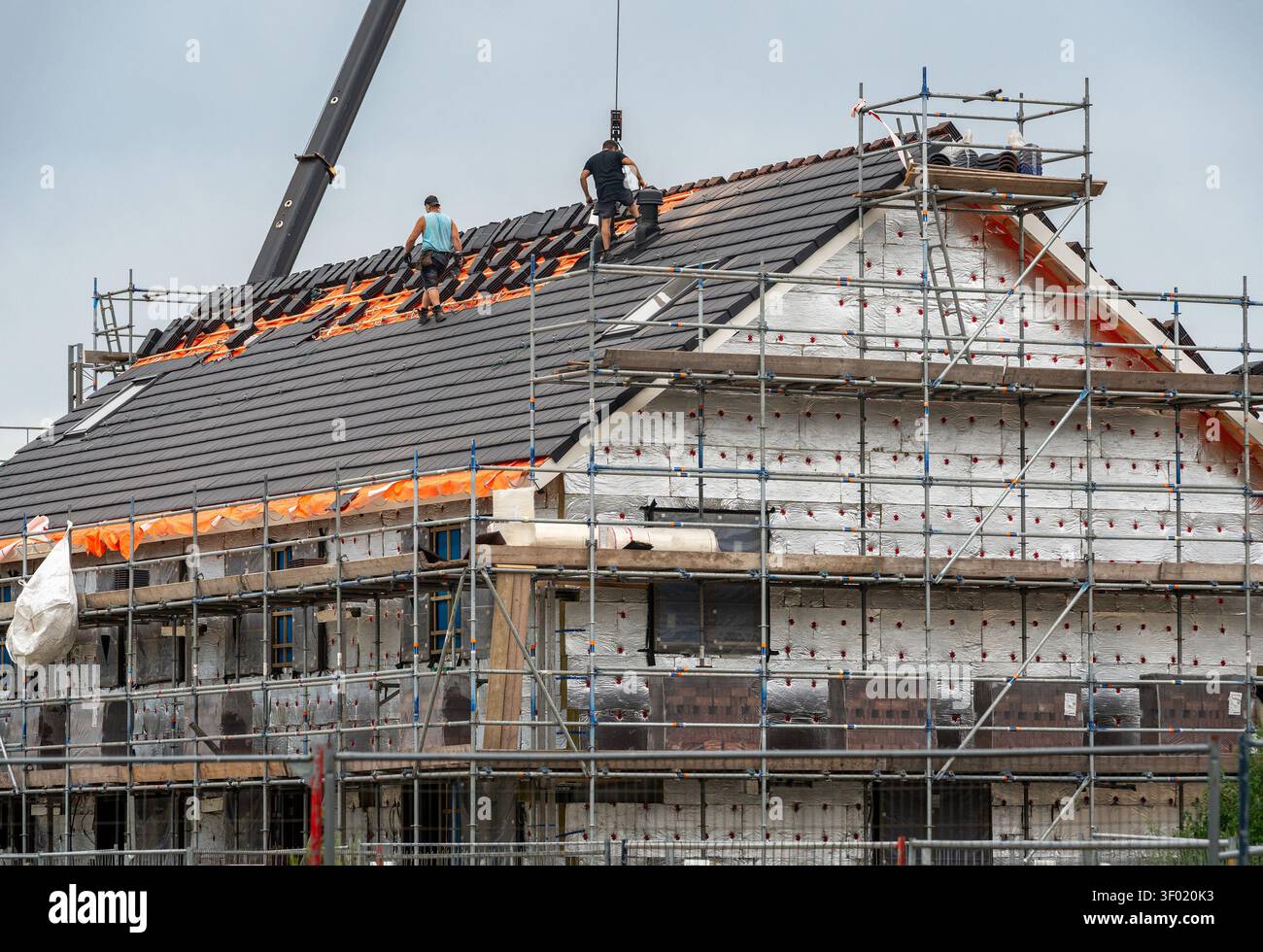 Installazione di tetti di tegole in nuova casa in costruzione, lavori di tetti con costruttori e ponteggi Foto Stock