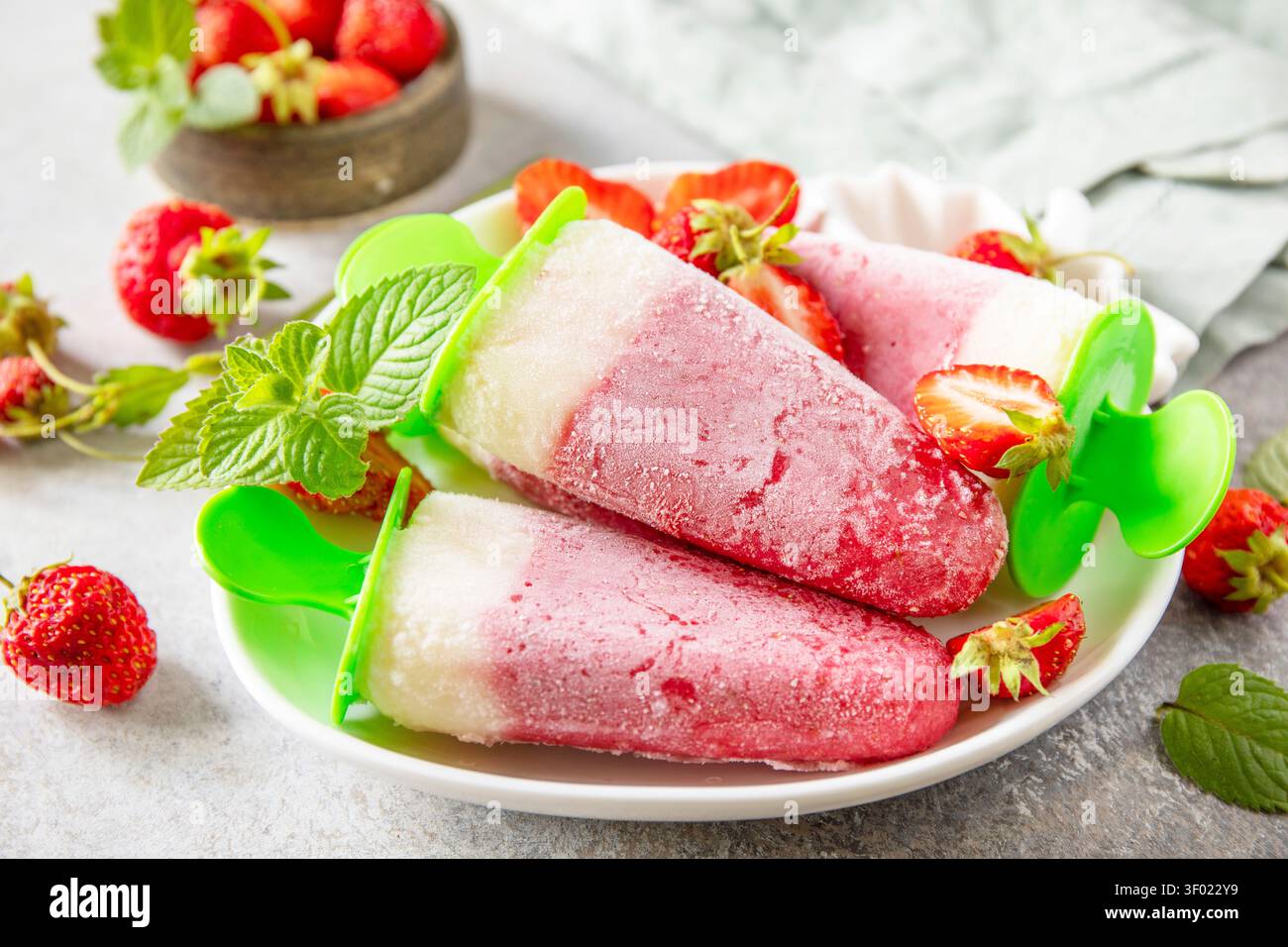 Gelato alle fragole fatto in casa su un bastoncino a base di fragole fresche su una superficie di pietra grigia testurizzata. Gustoso dessert estivo pronto da mangiare. Foto Stock