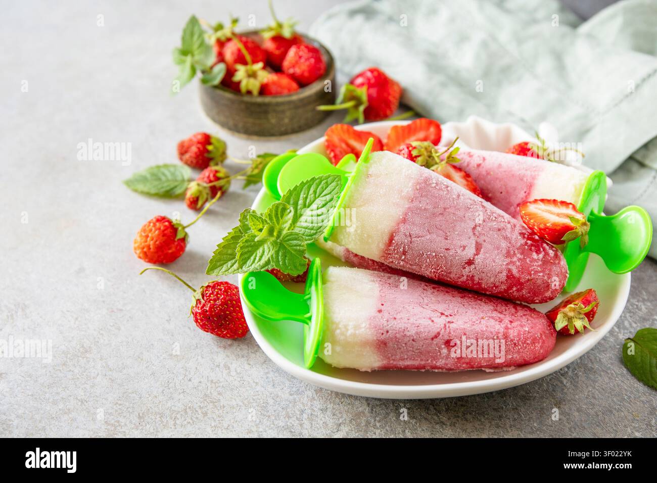 Gelato alle fragole fatto in casa su un bastoncino a base di fragole fresche su una superficie di pietra grigia testurizzata. Gustoso dessert estivo pronto da mangiare. Copia spazio. Foto Stock
