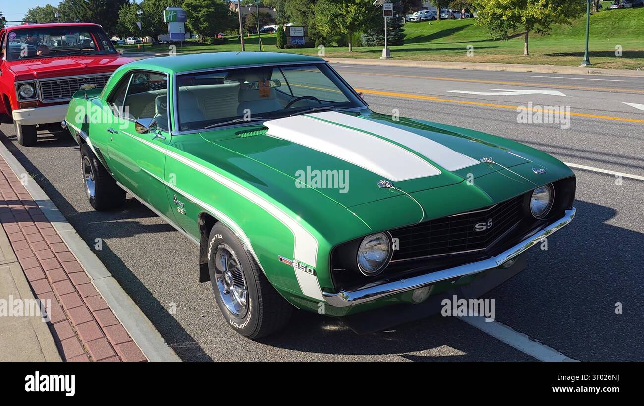 Una classica e vivace muscle car verde con strisce bianche sul cofano, che guida su una strada soleggiata in una mostra automobilistica. Foto Stock