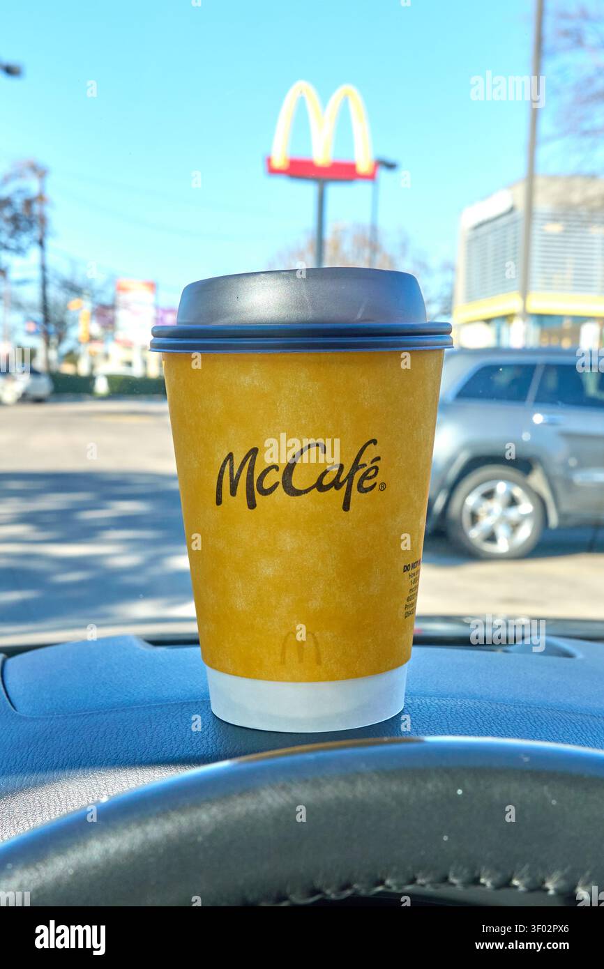 DALLAS, Texas, USA - 16 FEBBRAIO 2024: Una tazza di caffè McCafé è posizionata in modo prominente sul cruscotto di un'auto di fronte a un ristorante McDonald's. La tazza gialla, Foto Stock