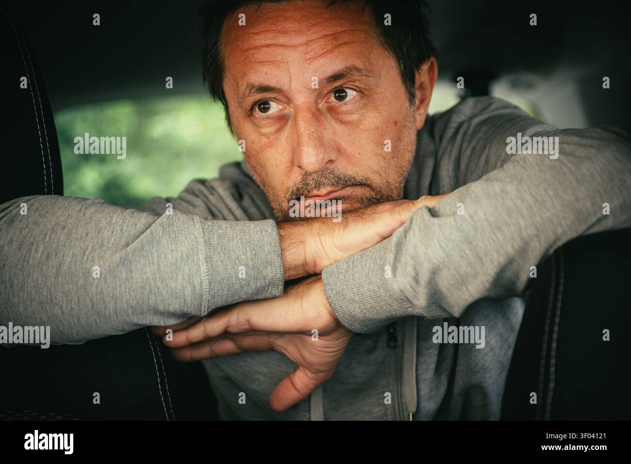 Un uomo di mezza età si appoggia su un seggiolino per auto, guardando in lontananza con un'espressione preoccupata e premurosa. Moody, ritratto introspettivo che trasporta t Foto Stock