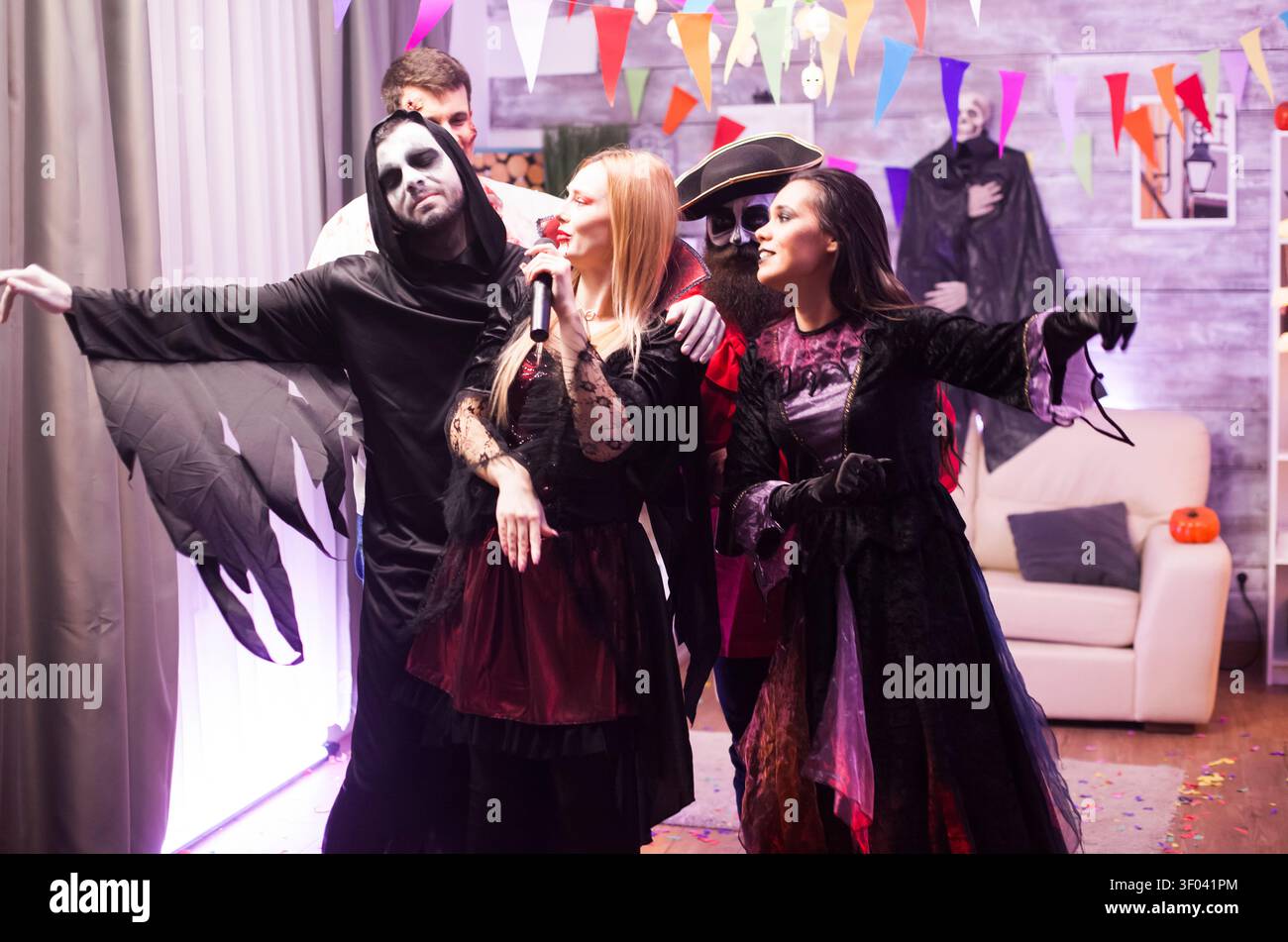 Un'attraente donna vampira canta con gli amici durante una festa di Halloween, aggiungendo energia vivace alla festa in costume. Foto Stock