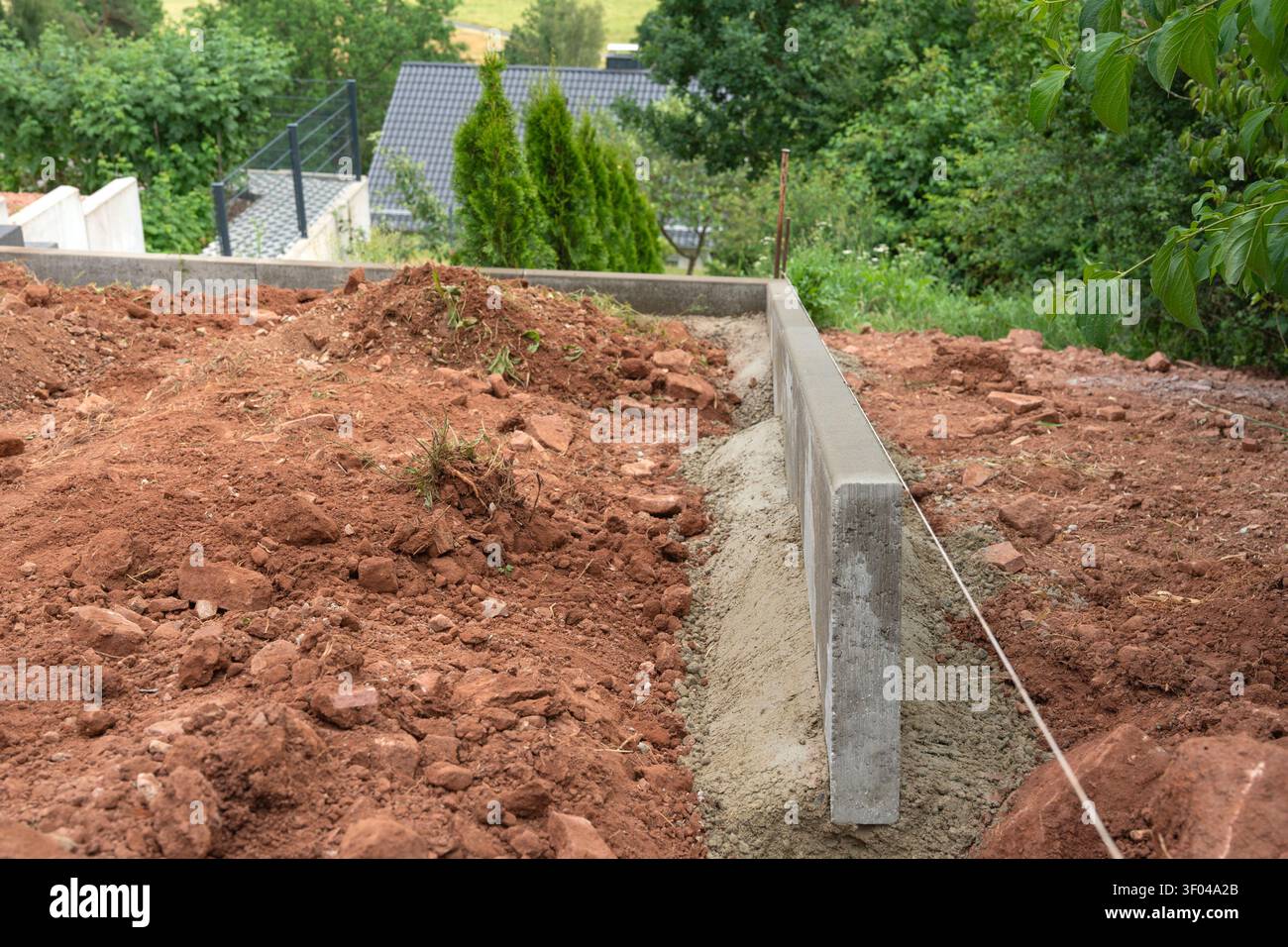 Costruzione di fondazioni in calcestruzzo in corso, in zona residenziale, con blocchi di cemento, terreno rosso, verde, con calcestruzzo, consistenza del terreno, da a. Foto Stock