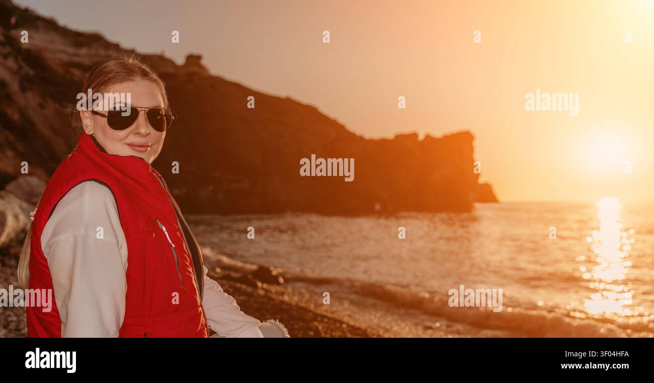 Donna al tramonto sulla spiaggia che sorride su una spiaggia rocciosa durante un'ora d'oro al tramonto sul mare con le montagne Foto Stock