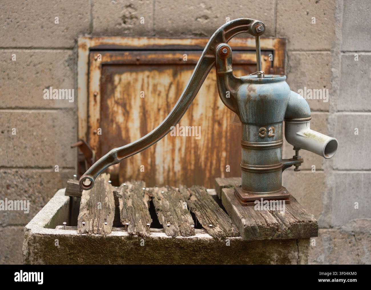 Vecchia pompa dell'acqua manuale in ghisa resistente agli agenti atmosferici montata su un bacino in pietra rustica fuori da un muro, Kyoto, Giappone Foto Stock