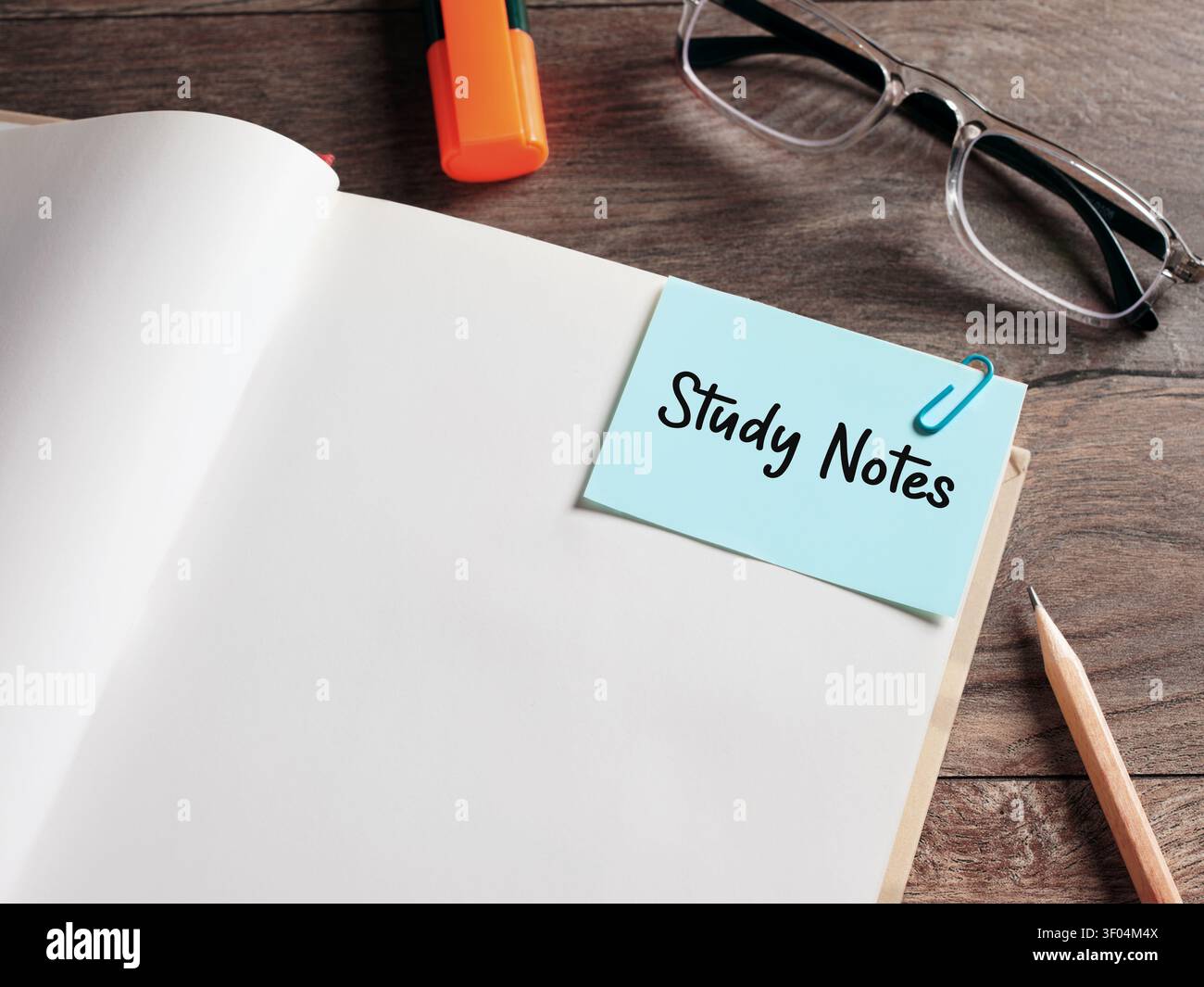 Testo di appunti di studio su un foglio di appunti attaccato a un libro aperto su una scrivania di legno. Foto Stock