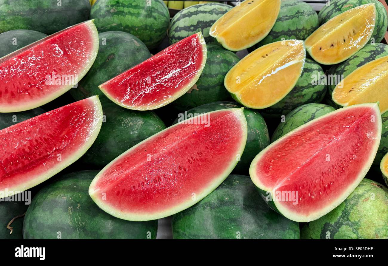 Fette di anguria rosse e gialle disposte su angurie intere in una esposizione di mercato. Sfondo alimentare con spazio per la pubblicità di generi alimentari, Foto Stock