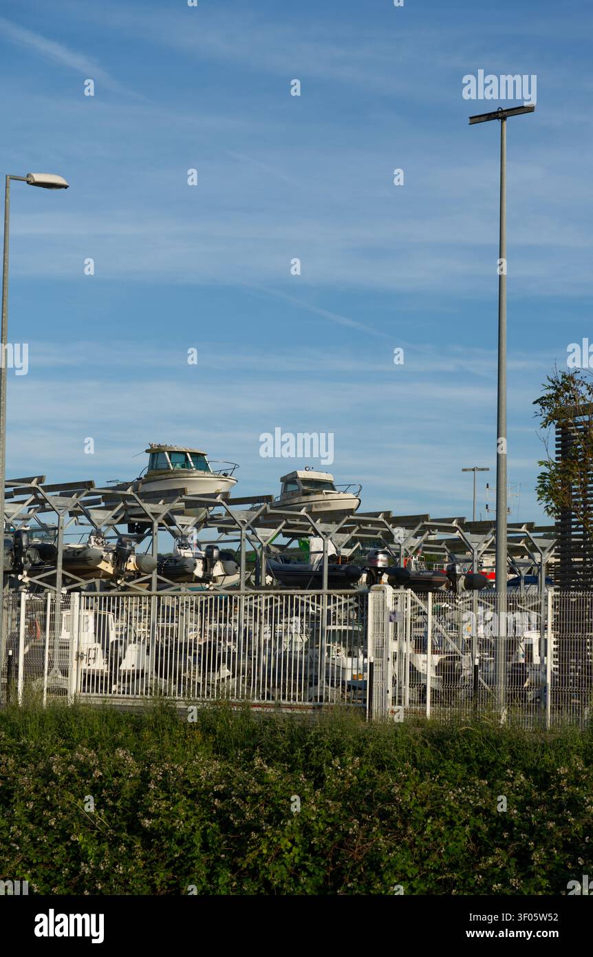 Diverse barche sono riposte su rack metallici all'interno di un'area portuale recintata, disposte su due livelli verticali per un uso efficiente dello spazio. Foto Stock
