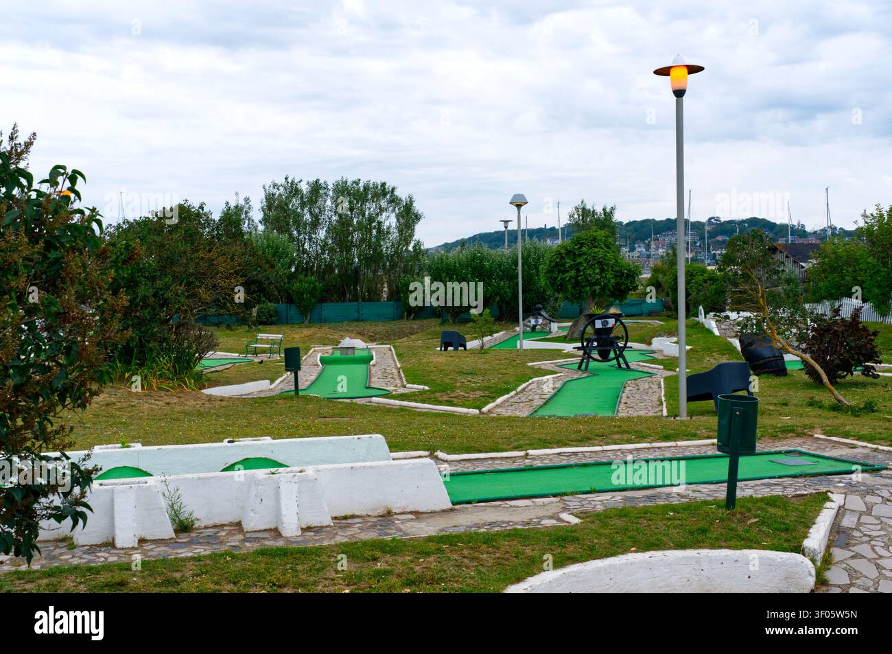 Un luminoso campo da mini golf all'aperto con più putting green, bordi in cemento bianco, vialetti in pietra e ostacoli giocosi. L'area è circondata Foto Stock