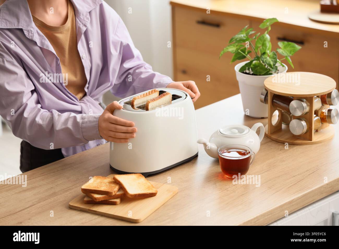 Persona che prepara toast con tostapane bianco in cucina Foto Stock