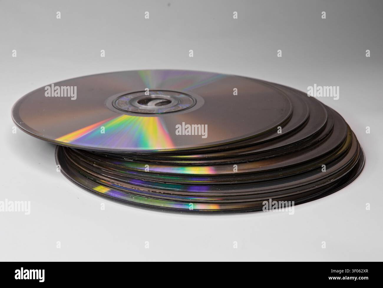 Pila di CD e DVD su una superficie bianca pulita, che mostra supporti ottici riflettenti, archiviazione dati e concetti di tecnologia obsoleti. Foto Stock