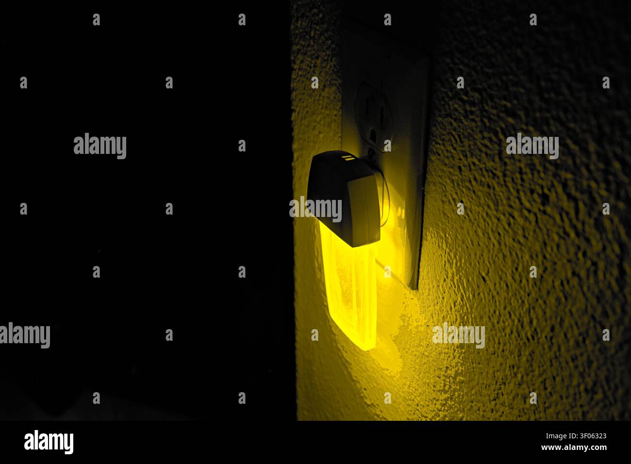Luce notturna gialla che brilla da una presa a muro in un interno buio, trasmettendo un'illuminazione ambientale calda, sicurezza notturna e comfort domestico. Foto Stock