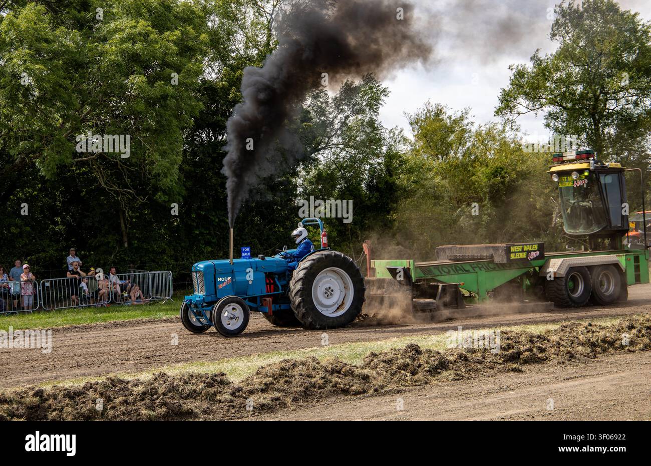 Un trattore Ford blu vintage che partecipa a una competizione di traino, emette un denso fumo nero dal tubo di scarico mentre trascina una slitta pesante Foto Stock