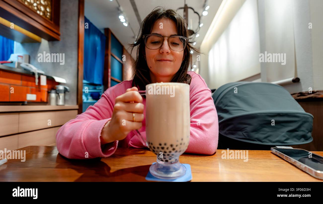 Una donna gode di un grande bicchiere di bollicine tea in un intimo caffè a Taichung, Taiwan. Gli interni moderni e l'illuminazione calda creano un'atmosfera rilassante Foto Stock