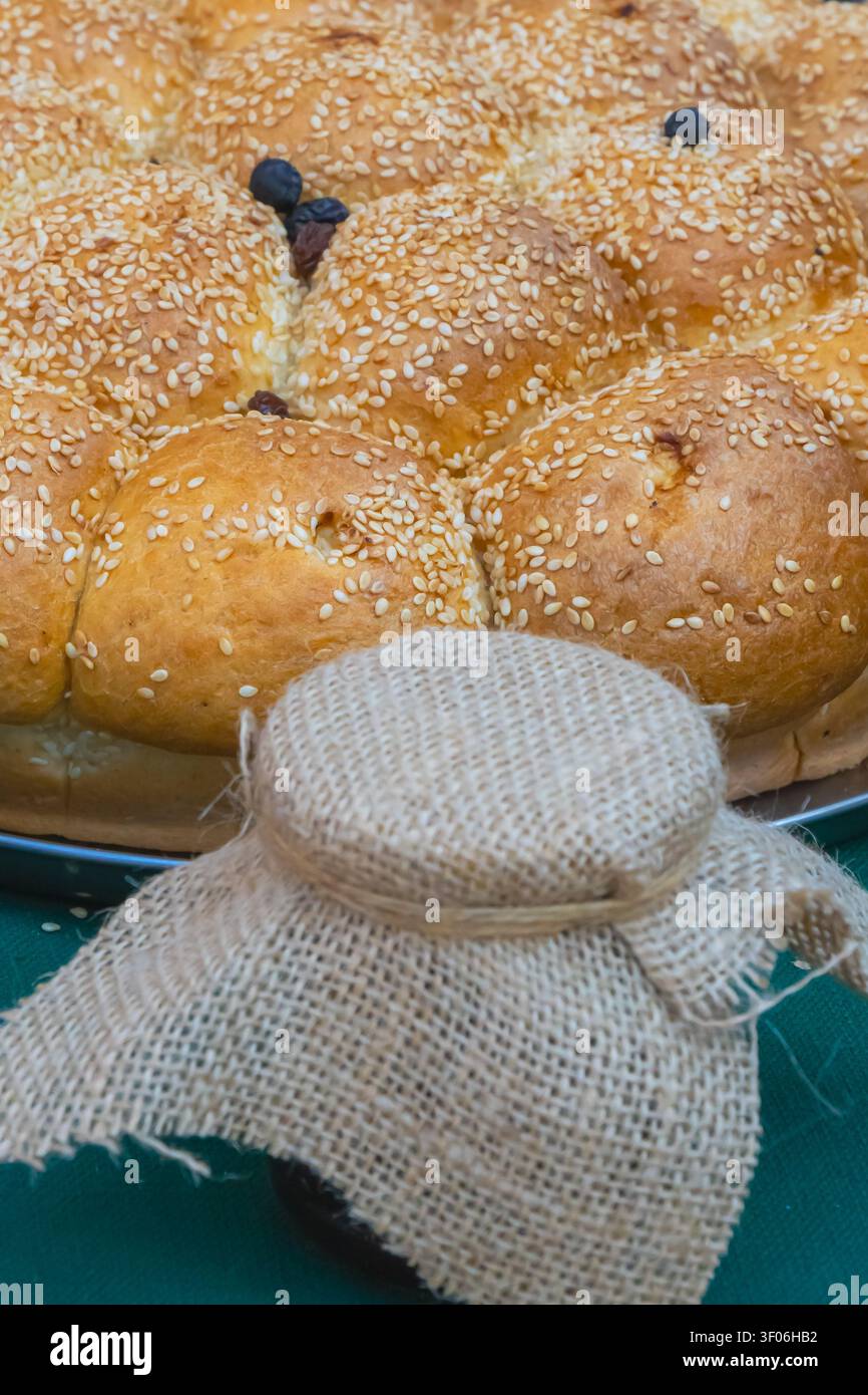 Prima di un pane dolce intrecciato tradizionale ricoperto di semi di sesamo e marmellata di frutta rustica fatta in casa in un vasetto di vetro, presentato in una panetteria festosa Foto Stock