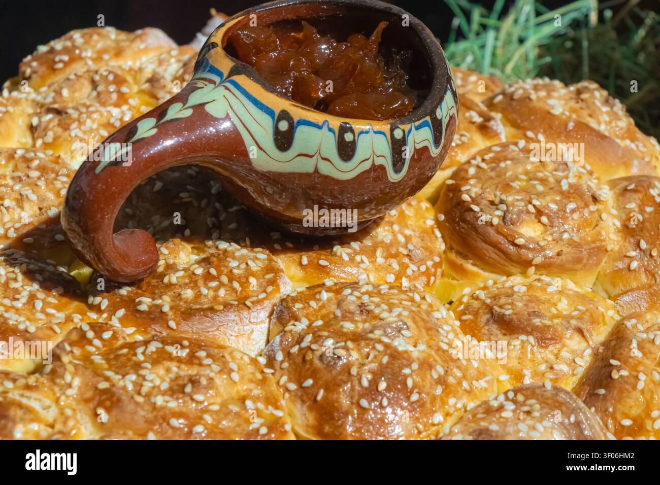 Pane dolce tradizionale ricoperto di semi di sesamo e servito con marmellata di frutta in una ciotola di ceramica rustica, creando una panetteria fatta in casa autentica e balcanica Foto Stock