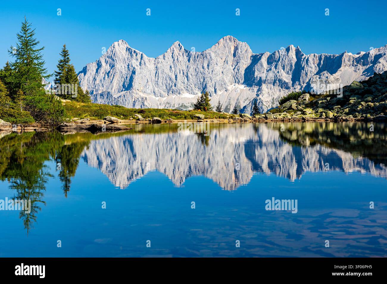 Le iconiche montagne del Dachstein si riflettono perfettamente nelle acque calme del lago Spiegelsee in una limpida giornata di sole. Paesaggio alpino pittoresco in Austria Foto Stock