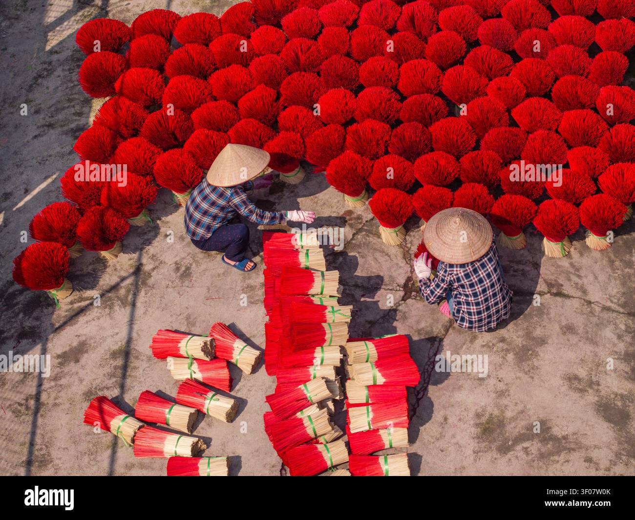 Vista aerea dei lavoratori che indossano i tradizionali cappelli conici mentre asciugano i bastoncini di incenso rosso brillante per terra in Vietnam. Foto Stock