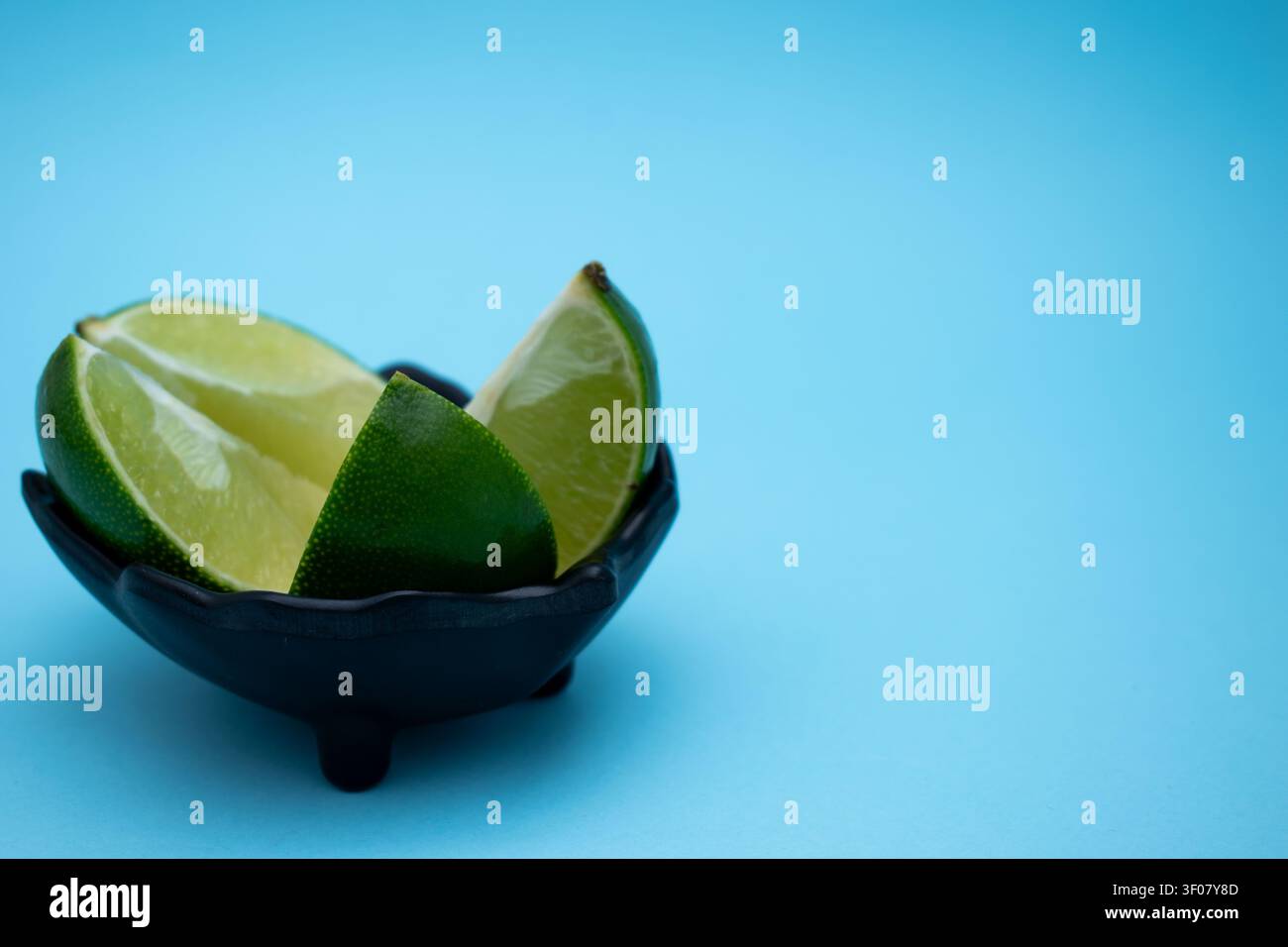 Fette di lime fresche in una ciotola nera su sfondo blu Foto Stock
