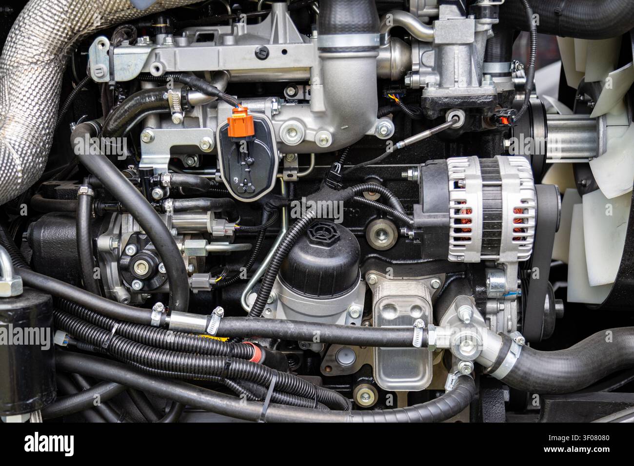 Assemblaggio del motore di una macchina agricola che mostra alternatore, tubi flessibili, condotte, cablaggio e componenti montati. La struttura meccanica comprende condotte di fluido Foto Stock