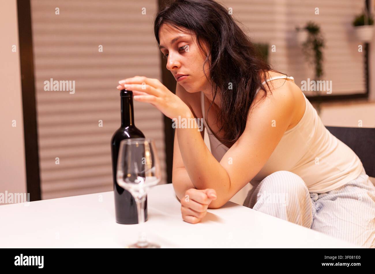 Donna triste che beve da sola in cucina Persona infelice che soffre di emicrania, depressione, malattia e ansia, si sente esausta con sintomi di vertigini e ha problemi di alcolismo. Foto Stock