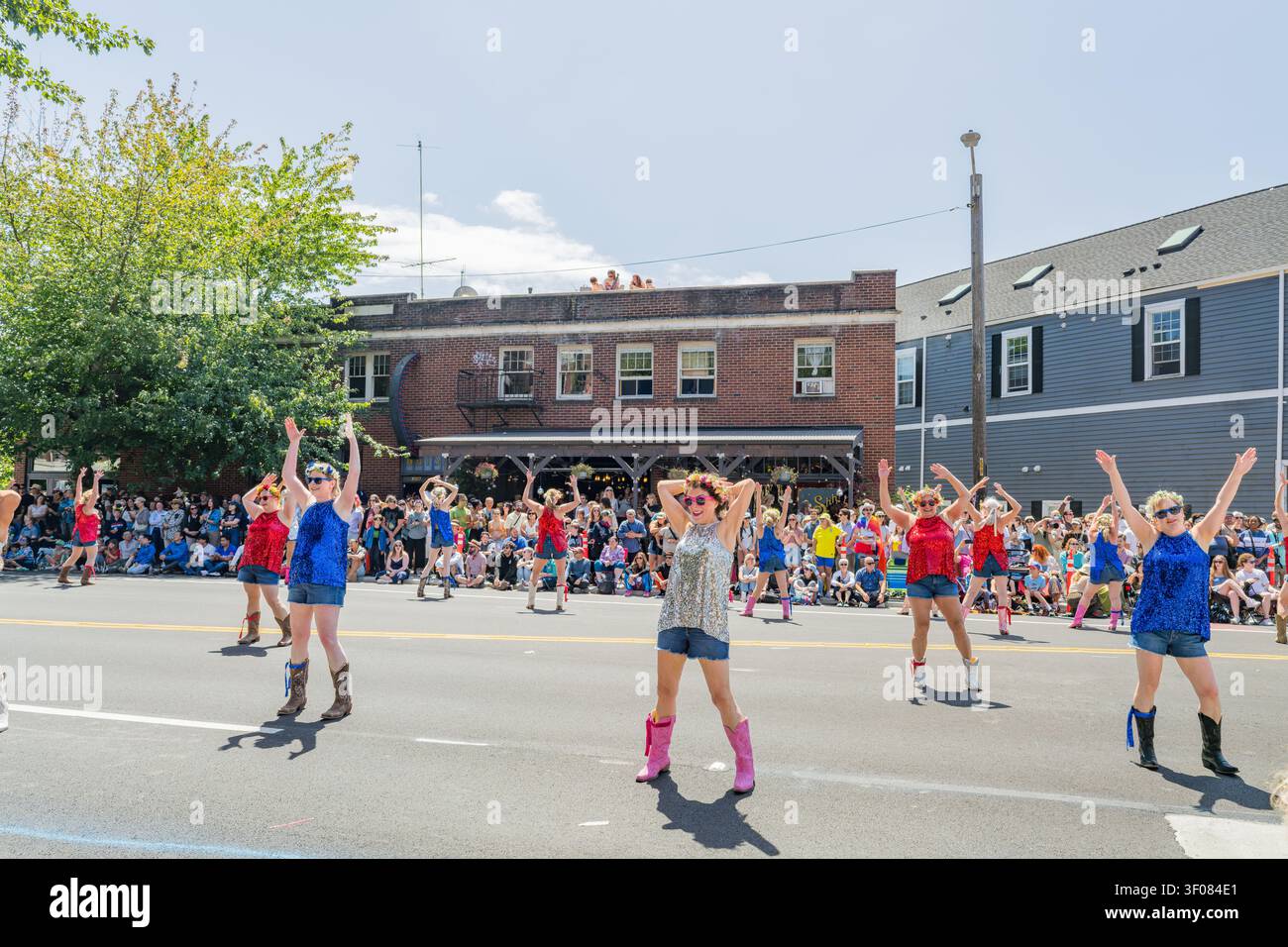 Stato di Washington, Stati Uniti, 20 GIU 2026 - Un gruppo di ballerini con top paillettati e pantaloncini di jeans eseguono una coreografia su una strada lastricata Foto Stock