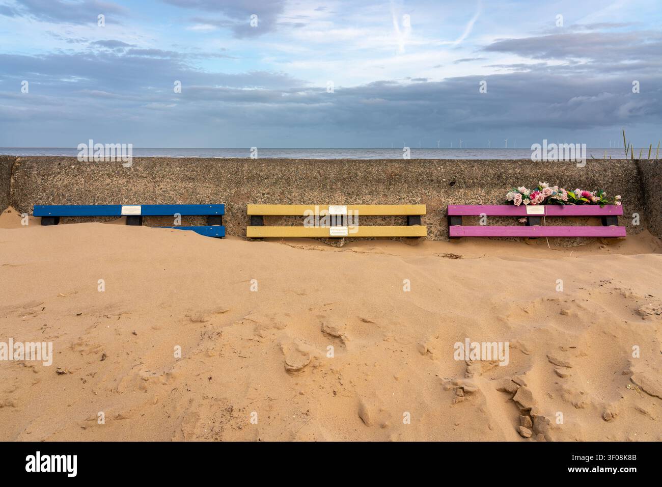 Panchine blu, gialle e rosa parzialmente sepolte dalla sabbia mobile Foto Stock
