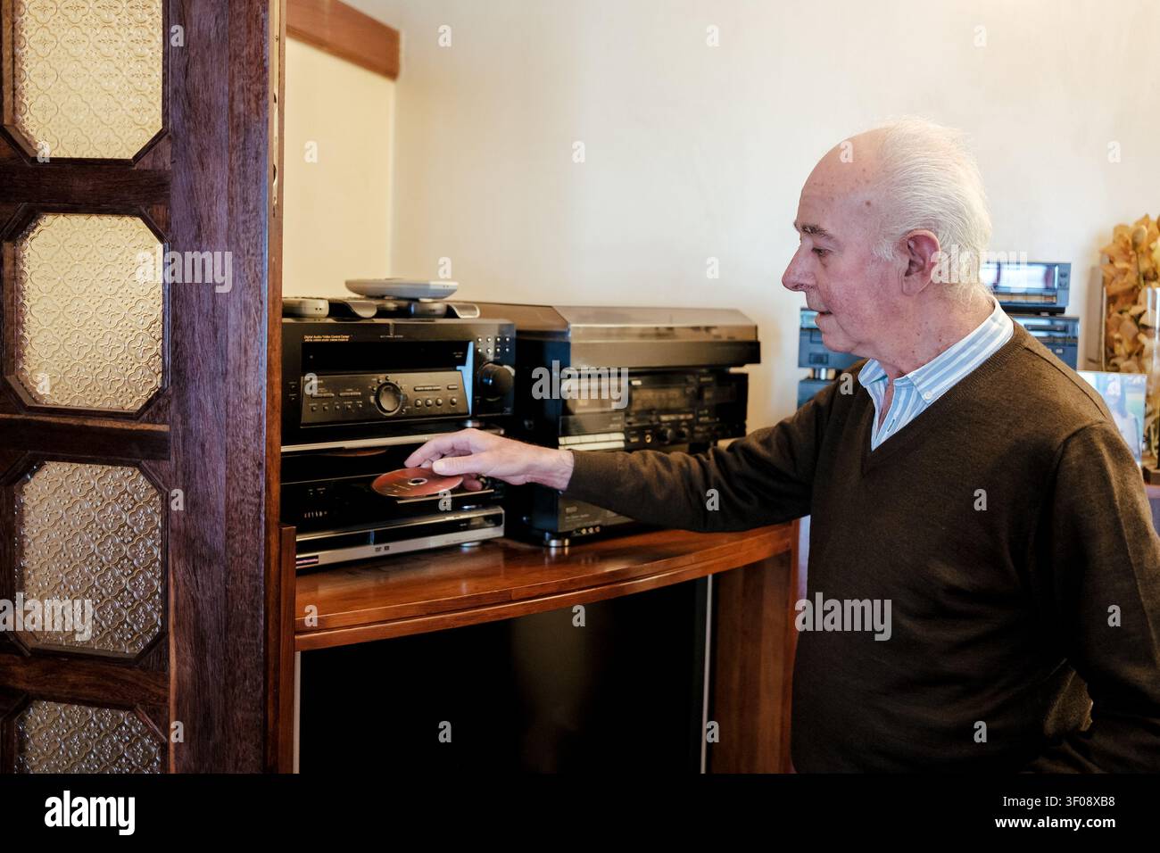 Uomo anziano che inserisce un compact disc in un lettore audio a casa Foto Stock