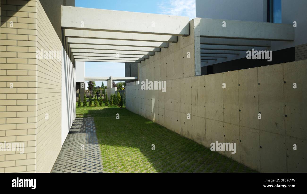 Architettura moderna che stabilisce un percorso strutturato con travi in calcestruzzo, lastroni di erba e ombre forti in una giornata di sole Foto Stock