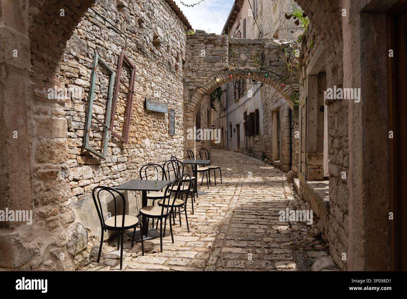 viale di ciottoli sereno con area seduta vuota negli edifici storici in pietra, prospettiva in prima persona dal viale, invitante e nostalgico Foto Stock