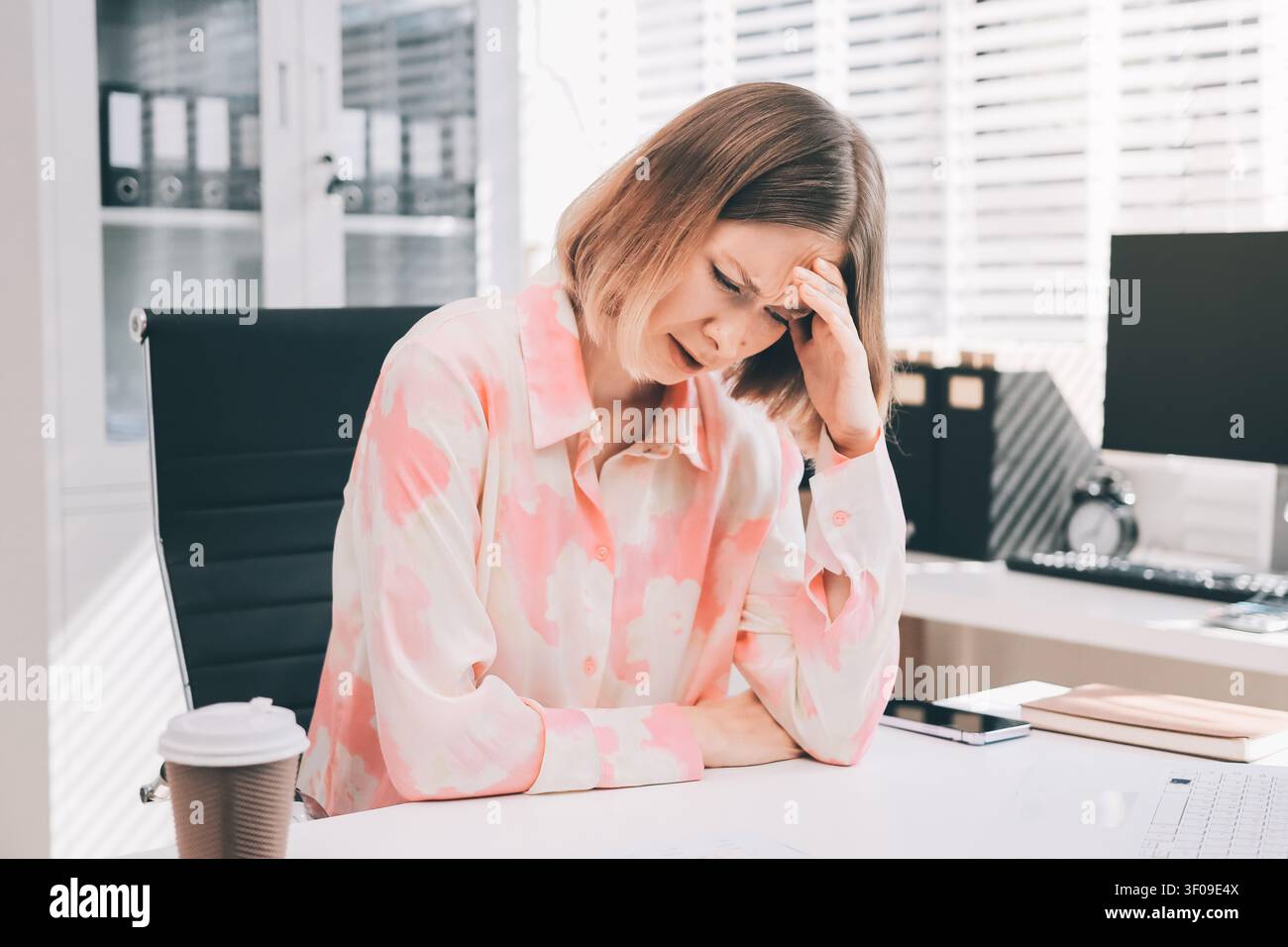 Giovane donna professionista che soffre di mal di testa mentre analizza grafici e grafici finanziari al computer, sperimentando stress correlato al lavoro nel moderno o Foto Stock