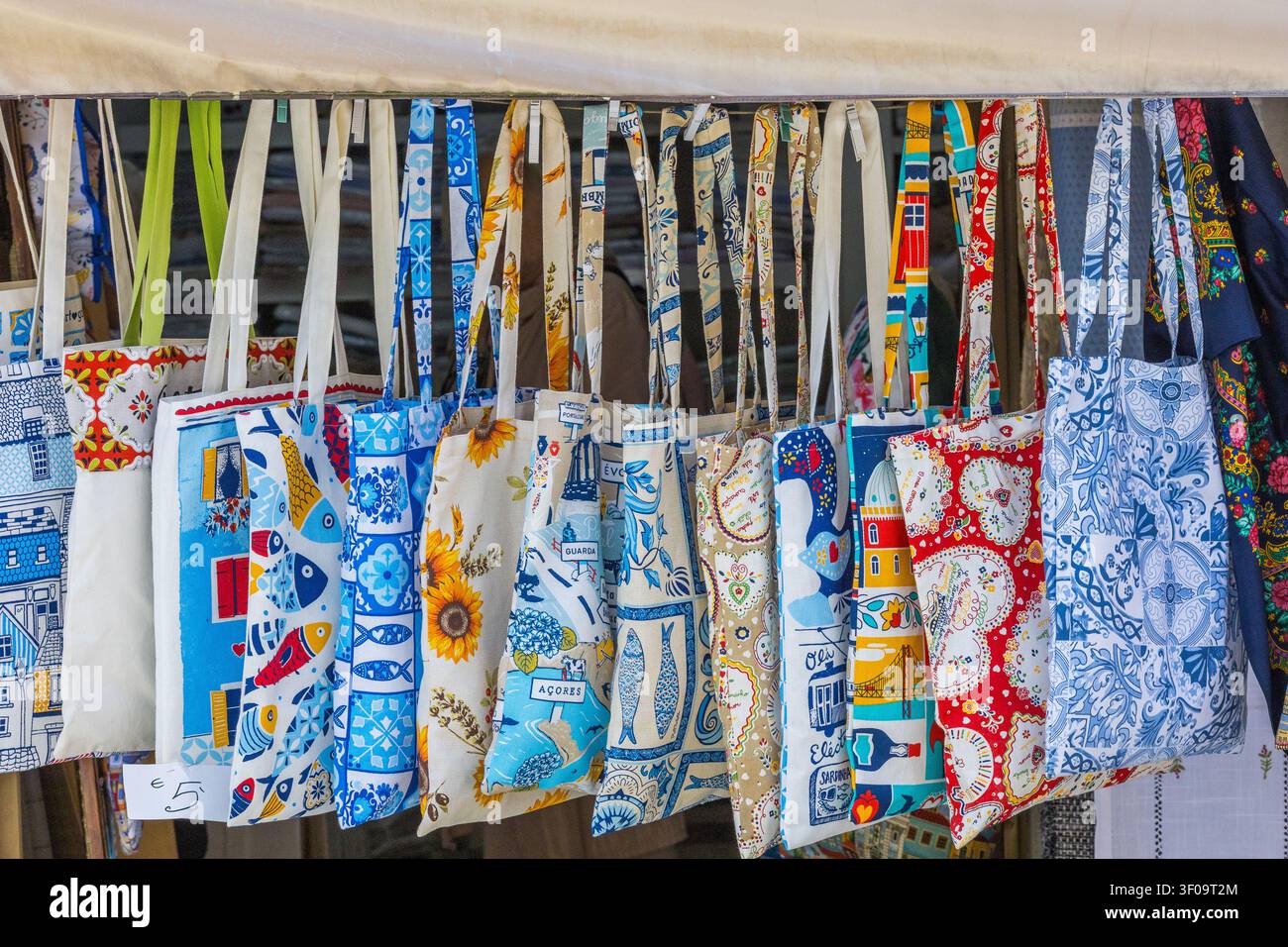 Una vivace esposizione di borse tradizionali portoghesi con motivi colorati, piastrelle e temi culturali è appesa a una bancarella del mercato di strada. Foto Stock