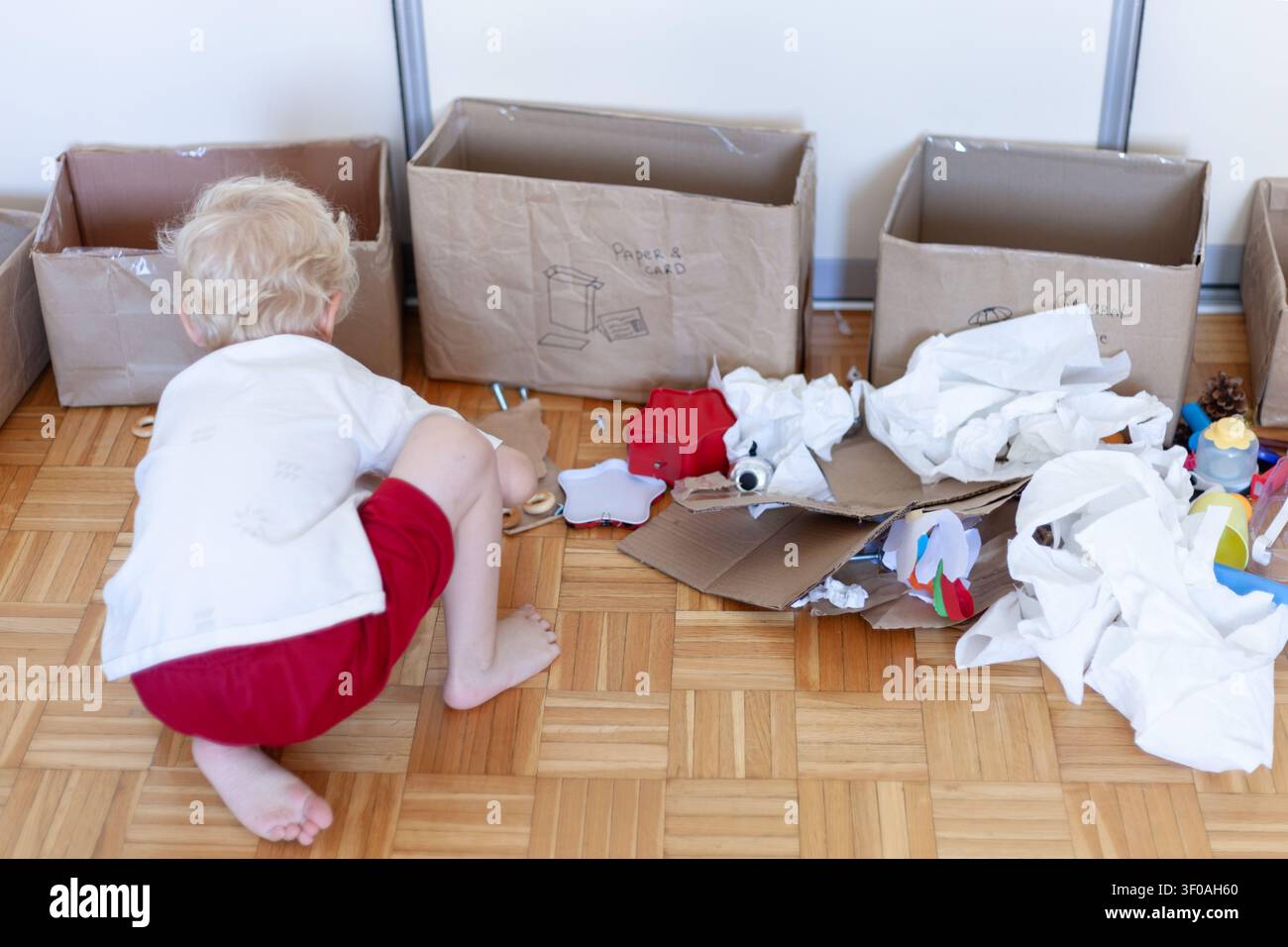 Bambino che prepara oggetti domestici prima di smistare i rifiuti nei contenitori del riciclo. L'educazione ambientale precoce inizia con azioni quotidiane. Foto Stock