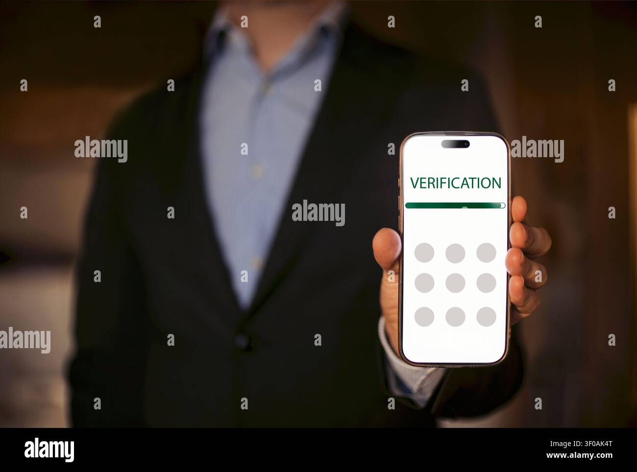 Uomo vestito con un completo nero presenta uno smartphone che mostra uno schermo di verifica con campi di input circolari, lo sfondo appare sfocato e in interno Foto Stock