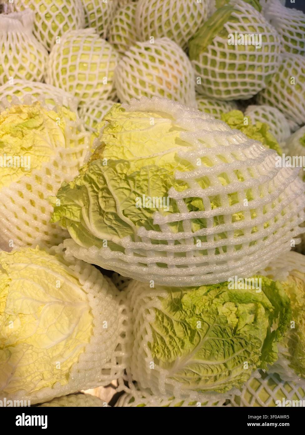 Cavolo cinese fresco avvolto in reti di schiuma bianca in un mercato. - Immagine stock catturata con smartphone