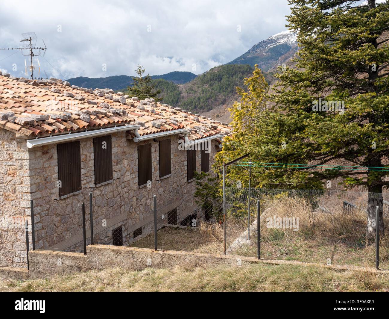 Una casa rurale rustica costruita in pietra naturale con un tetto classico di tegole, dotata di pietre posate sulla parte superiore per la protezione dal vento. L'edificio è situato in Foto Stock