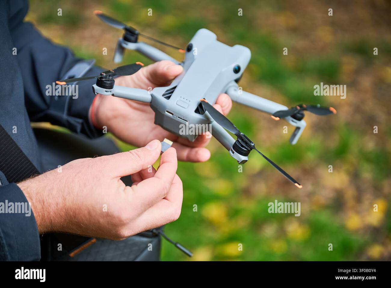L'uomo inserisce la scheda di memoria nel drone prima del volo. Primo piano delle mani posizionamento della scheda microSD in un quadricottero nel parco, preparazione del dispositivo per la registrazione, concetto di tecnologia moderna e videografia aerea Foto Stock