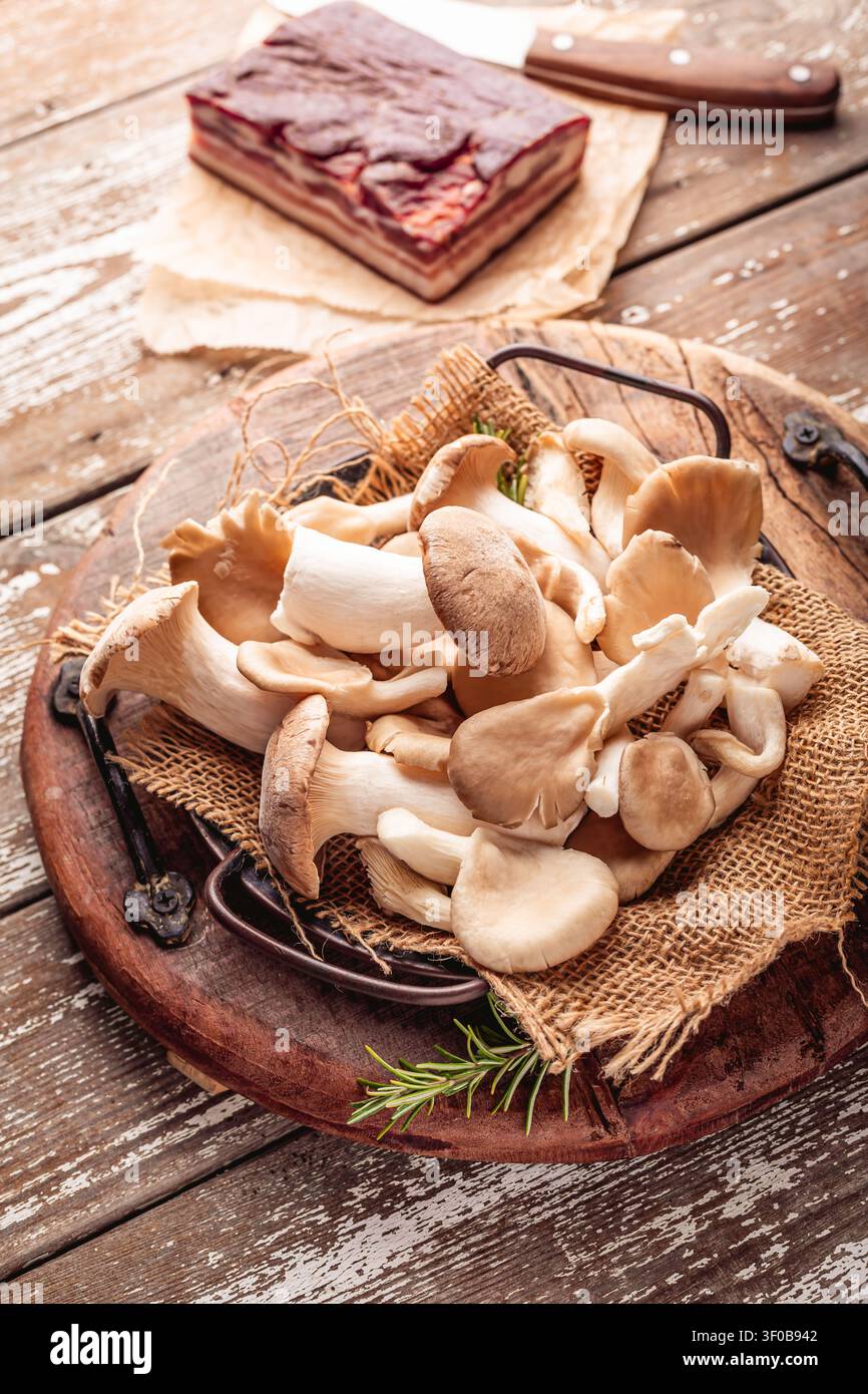 Funghi di ostriche appena raccolti e pancia di maiale stagionata su un rustico tavolo di legno Foto Stock