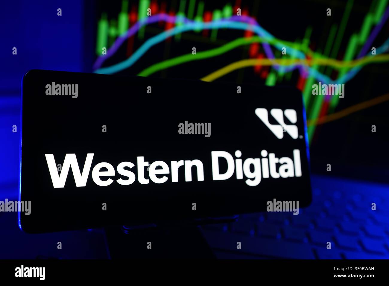 Logo della Western Digital Corporation visualizzato sullo schermo di uno smartphone davanti a un computer che mostra grafici delle prestazioni finanziarie del mercato azionario Foto Stock