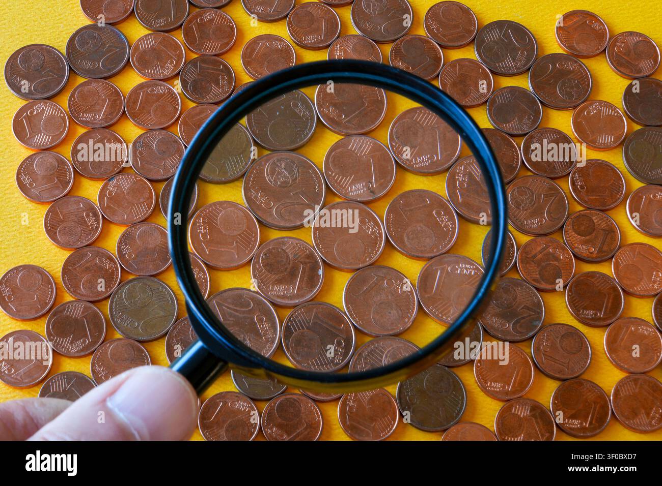 Lente d'ingrandimento che esamina monete da 1 e 2 centesimi di euro, illustrando la loro utilità, la possibile ritirata dalla circolazione e le tendenze dei pagamenti in contanti Foto Stock