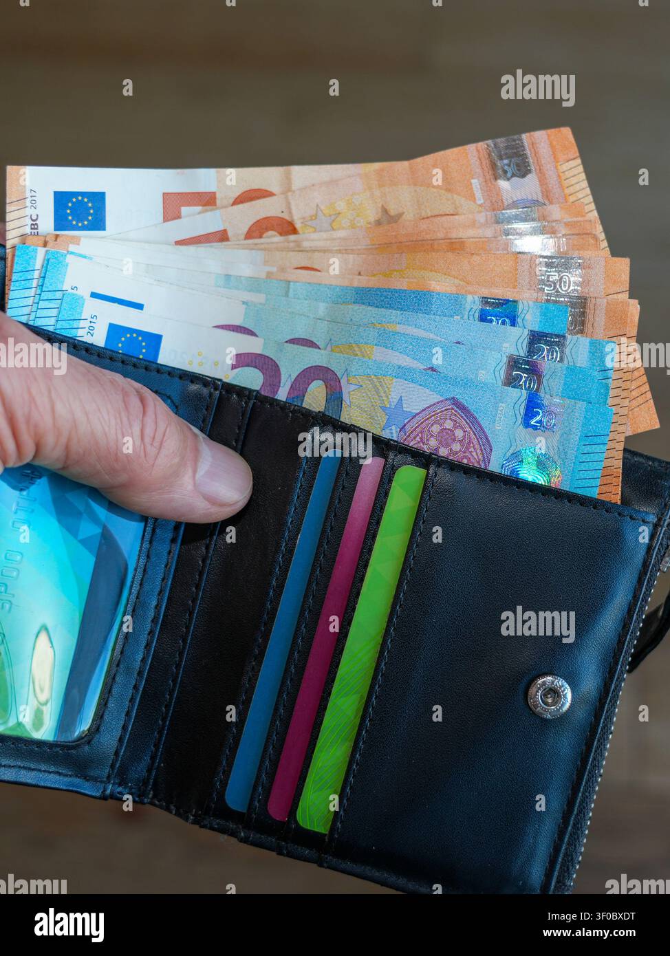 Primo piano di un portafoglio di pelle nero aperto pieno di banconote in euro e carte di pagamento, che simboleggia finanze personali, risparmi, budget e spese Foto Stock
