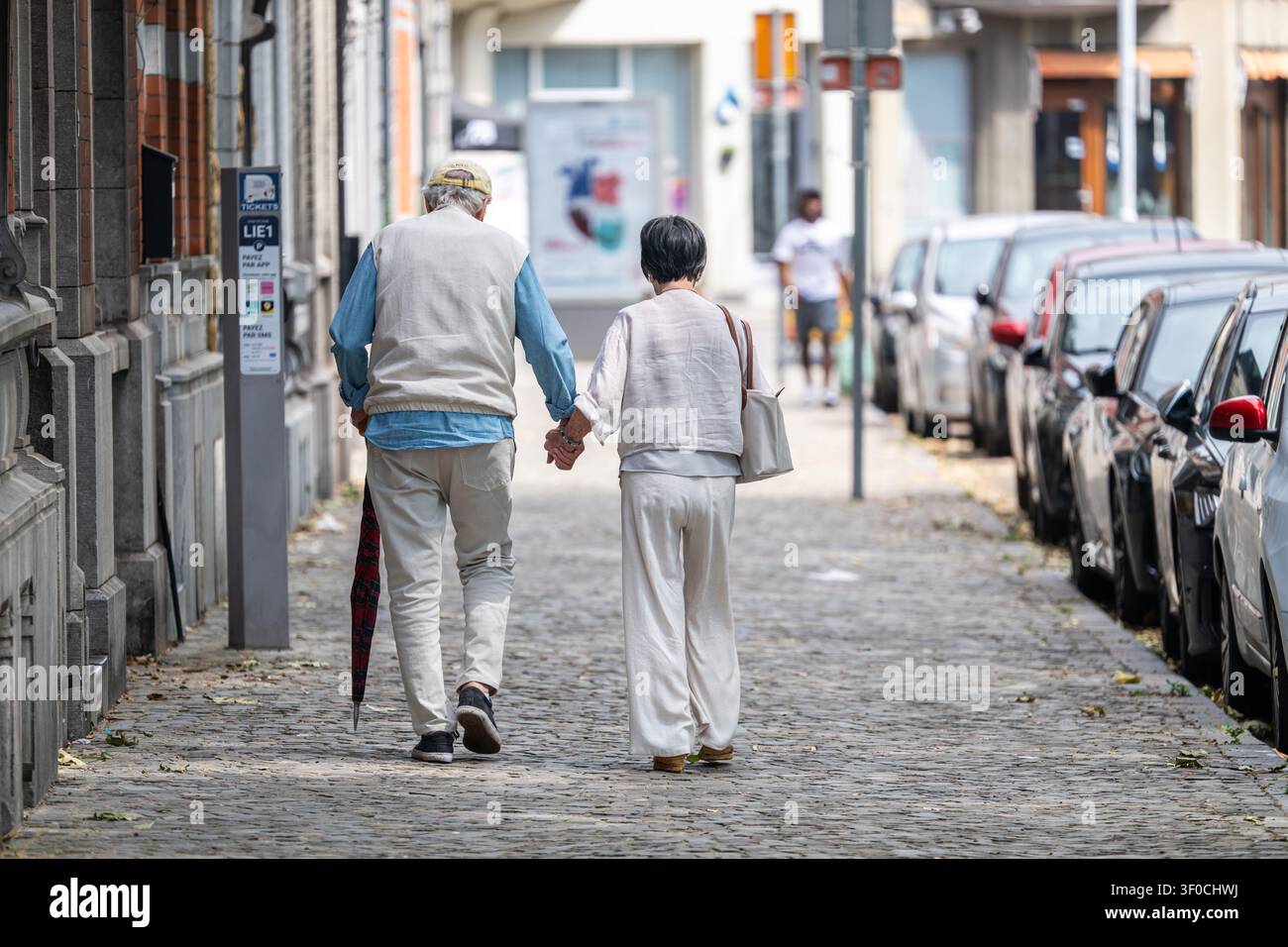 Una coppia anziana cammina mano nella mano lungo una strada acciottolata vicino a Place de l'Yser nel quartiere Outremeuse di Liegi, illustrando la vita quotidiana e un Foto Stock
