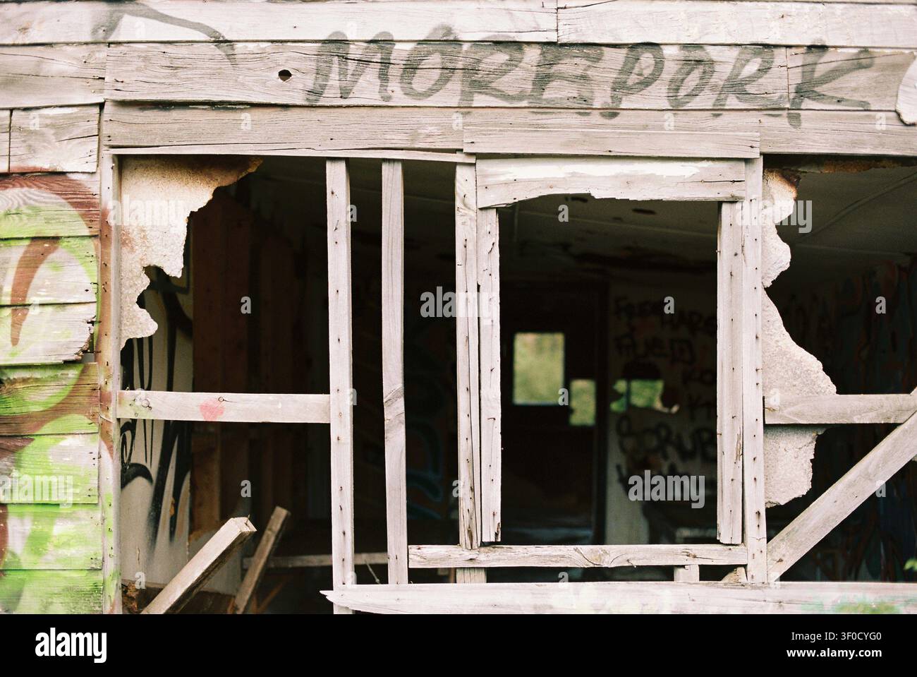 Una facciata in legno consumata di un edificio abbandonato con finestre rotte. Graffiti, tra cui "MOREPORK", sono visibili sulla struttura. Scatto su 35mm Port Foto Stock